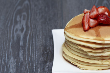 Stack of pancakes with strawberry on dark wooden background