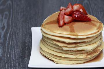 Stack of pancakes with strawberry on dark wooden background