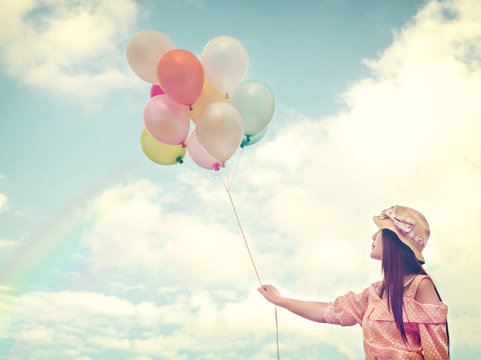 Vintage photo of  Happy young red hair woman  holding colorful balloons and flying on clouds sky background.