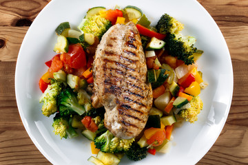 Grilled chicken fillet, breast with cooked vegetable Tomatoes, Carrots, Peppers, Courgettes, brocoli on plates.