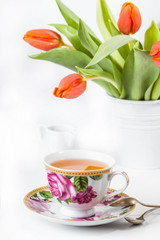 Fototapeta na wymiar Cup of tea with red tulips over white