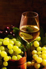 White wine and green grapes in a wicker basket in a wine cellar,