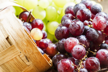 Purple round ripe grapes in a wicker basket on an old wooden bac