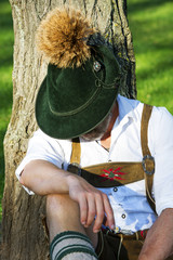 bavarian man sitting by a tree and sleeps