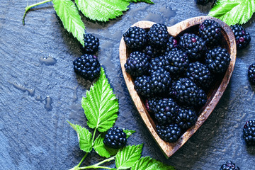 Fresh blackberries with green leaves in a bowl in the shape of a