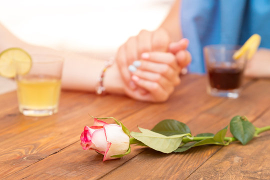 Concept trust and flower Heterosexual Couple Holding Hands of Each Other Expressing Love Trust Care Tenderness Rose Flower on Foreground Drinks Glass Decorated Fruits on Natural Wood Restaurant Table