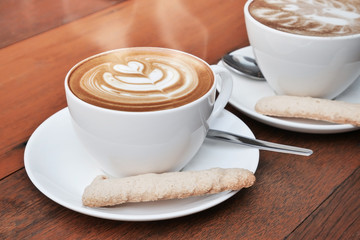 two cups of latte art coffee in a white cup on wooden background