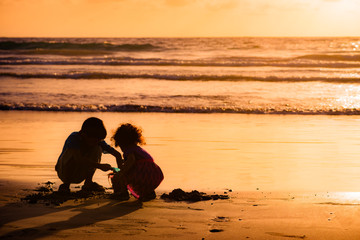 Children playing with sand by the sea at sunset in Tobago
