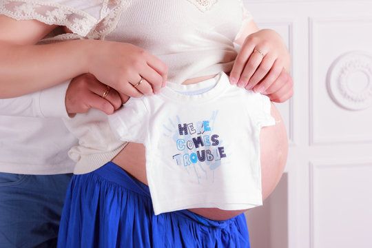 Pregnant woman's and man's hands holding a baby t-shirt 