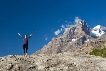 Young woman doing exercise Cute Girl Doing Yoga Fitness to Stretch Body Staying on High Rock at Mountain Panoramic Landscape Outdoor Sunny Sky Peaks Wilderness Country Smiling Beautiful Face Sunshine