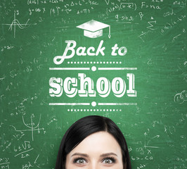 A forehead of the brunette girl and words: ' back to school ' which are written on the green chalkboard.