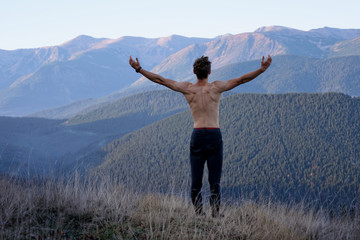 Fototapeta na wymiar Back view of a man at the top of the mountain with raised hands and muscles on the back