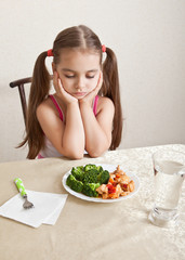 The girl looks indifferently at the dish with meat and broccoli