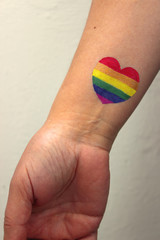 Young woman with a tattoo on his wrist heart painted in the colors of the rainbow