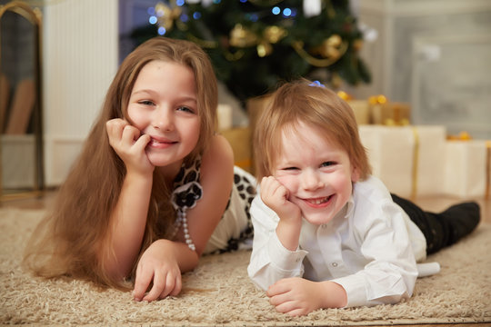 Cheerful girl and boy lying on the floor near a Christmas tree