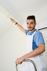 handsome young man professional painter applying white paint in wall with roller