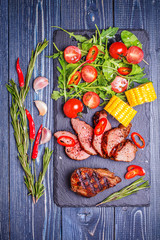 BBQ lamb steak with vegetable salad and corn on dark wooden back