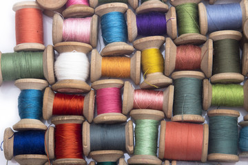 colored cotton thread for sewing on wooden spools on a white