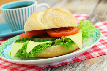 Cheese roll with lettuce, tomato and cucumber and cup of coffee
