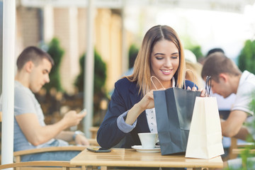 Portrait of happy young woman sitting in a cafe  and looking at her bags satisfied with the shopping