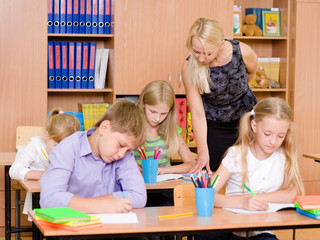 young teacher helps students of primary school in the exam