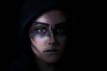 Girl in hoodie with scary face makeup on black background