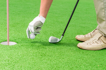 en's hand in a glove putting a golf ball near the hole
