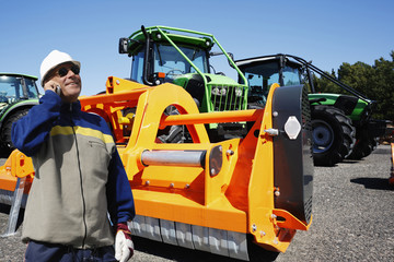 farmer talking in phone with large tactor and mower in background