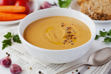 Vegetarian vegetable cream soup with eggplant and carrots in white bowl on wooden table, selective focus