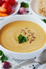 Vegetarian vegetable cream soup with eggplant and carrots in white bowl on wooden table, selective focus