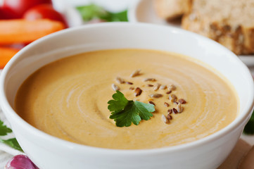 Vegetarian vegetable cream soup with eggplant and carrots in white bowl on wooden table, selective focus