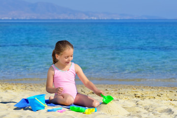Adorable toddler girl playing with her toys at the beach