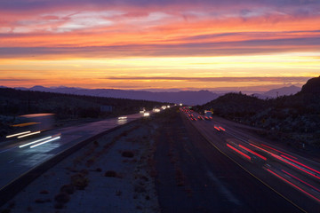 Cars drive Interstate 15 at sunset at California Nevada border looking west.