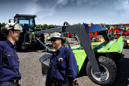 farmers, mechanics with giant plow and mower coupled to tractors