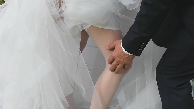 Leg of the bride. The bride and groom. Wedding. The groom stroking hand and touches the leg of the bride in white stocking. Sexy newlywed game. The intimate act of two lovers. White fluffy dress.