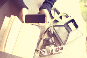 Girl's hands with cell phone, old camera and a book on a wooden