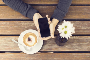 Girl keeping a cell phone and a cup of cappuccino on a wooden ta
