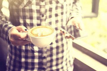 Hipster girl keeping a cappuccino and cell phone