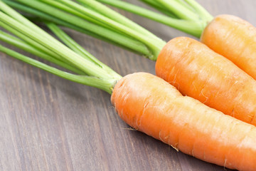 Raw carrots with green tops on wooden background