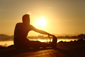 Silhouette of a fitness man stretching at sunset