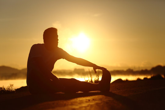 Silhouette of a fitness man stretching at sunset