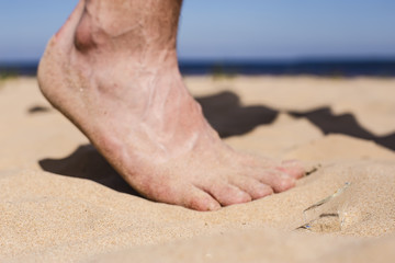 Man goes on the beach and the risk of stepping on a splinter of broken bottle glass, which is lying on the sand littered in places with poor environmental conditions. Side view, blurred foot.