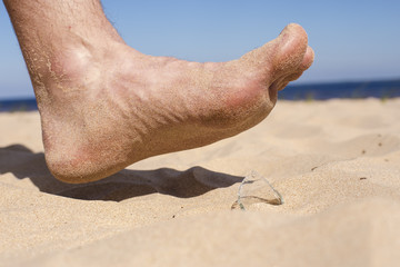 Man goes on the beach and the risk of stepping on a splinter of broken bottle glass, which is lying on the sand littered in places with poor environmental conditions. Side view