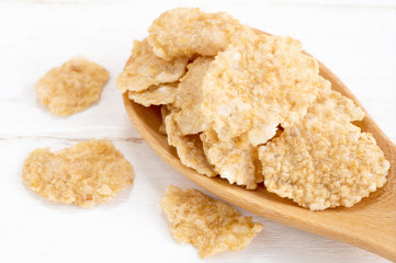whole wheat grain flakes  in wooden spoon on white wood backgrou