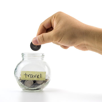 Hand putting coin into glass container with  travel label on white background.