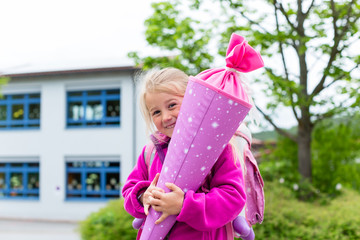 Schulkind am ersten Schultag mit Schultüte steht vor der Schule