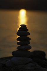 Stack of balanced pebbles, stones against colorful sunset by the sea