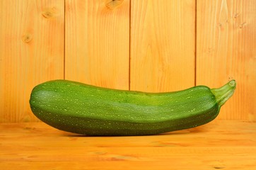 One green zucchini vegetable shown whole on a yellow wooden background. Space for text on the upper part of the image.