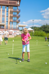 Cute little girl playing golf on a field outdoor. Summertime