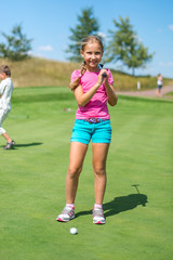 Cute little girl playing golf on a field outdoor. Summertime